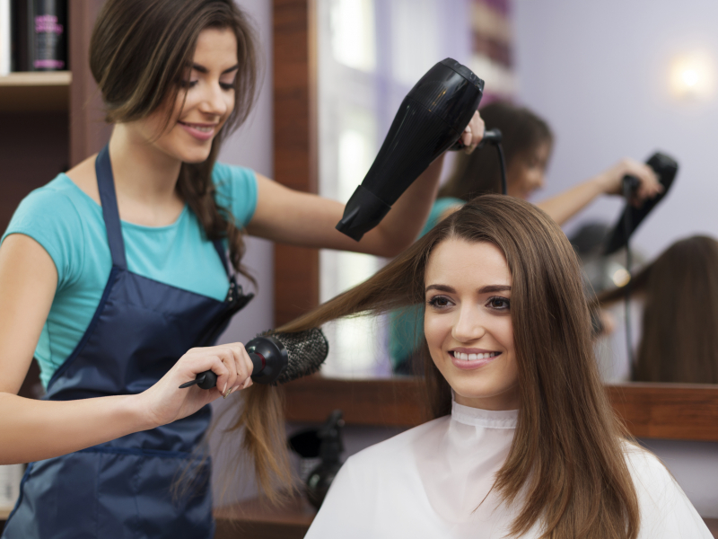 Female hairdresser using hairbrush and hair dryer